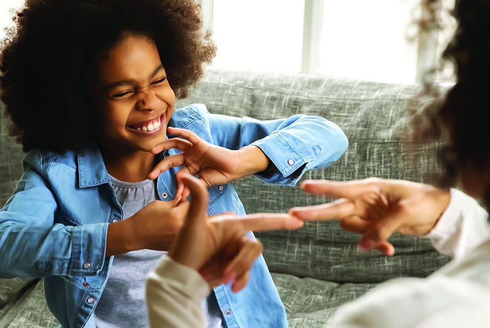 African deaf kid girl and her mother sitting on couch showing symbols with hands using visual-manual gestures enjoy communication at home. Hearing loss disability sign language learning school concept